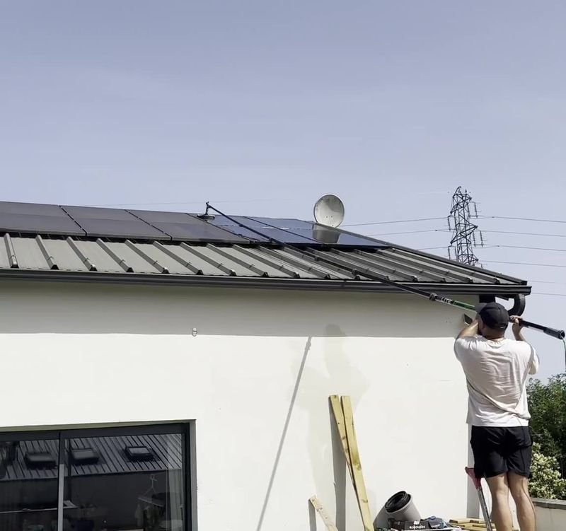 Nettoyage de panneaux solaires sur le toit d'une maison avec une perche télescopique à l'eau pure